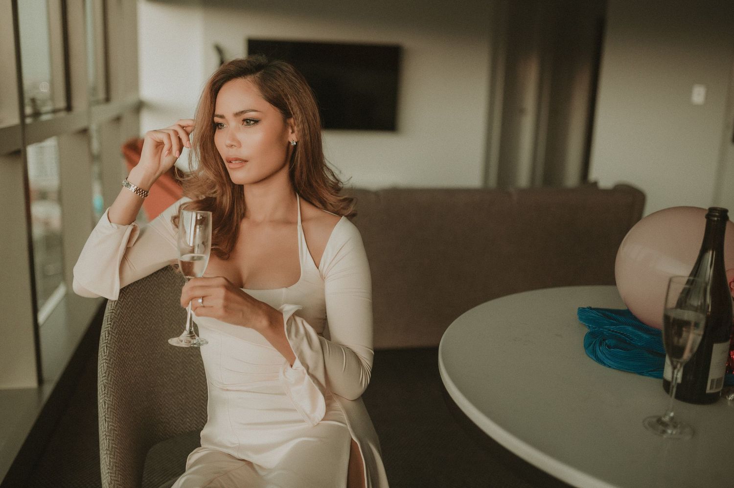 Person holding wine glass in white dress against interior setting.