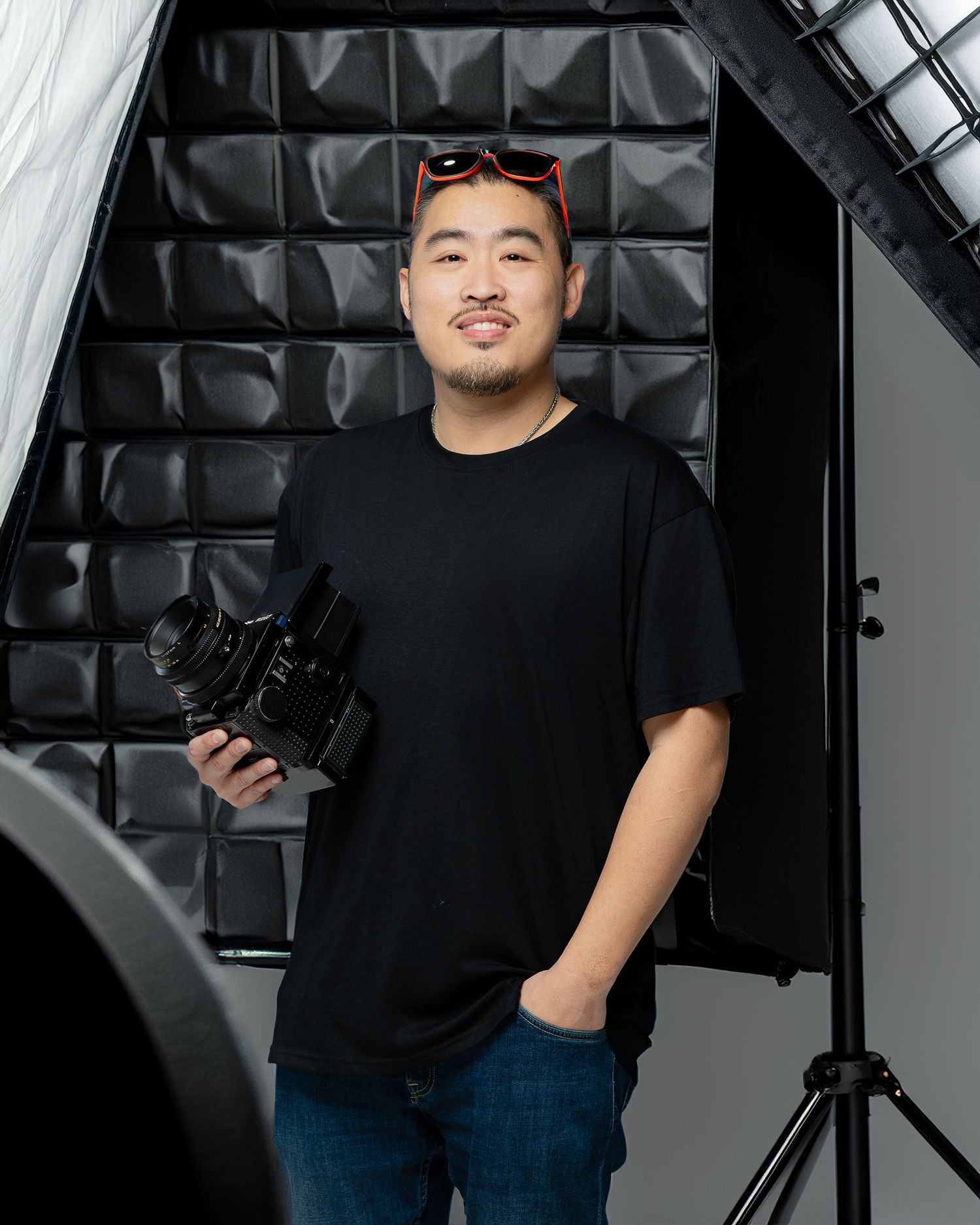 Professional photographer in a black t-shirt holds a camera while standing in a photo studio with lighting equipment.