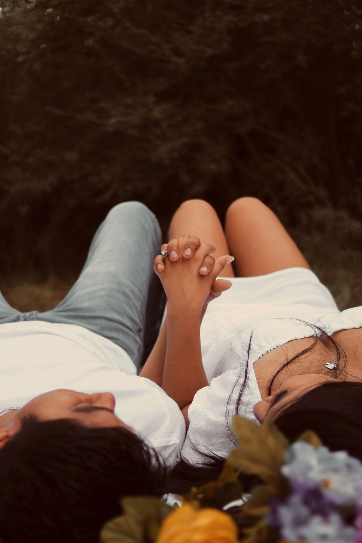 Couple holding hands while lying down together surrounded by flowers.