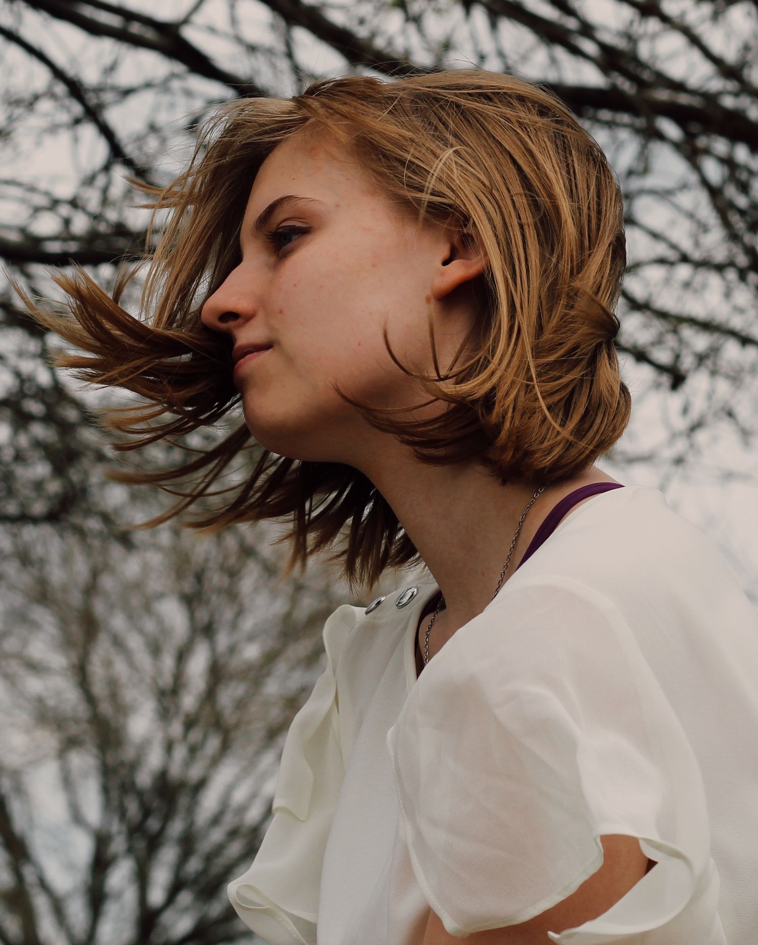 Dynamic side profile portrait of windswept hair against bare branches.