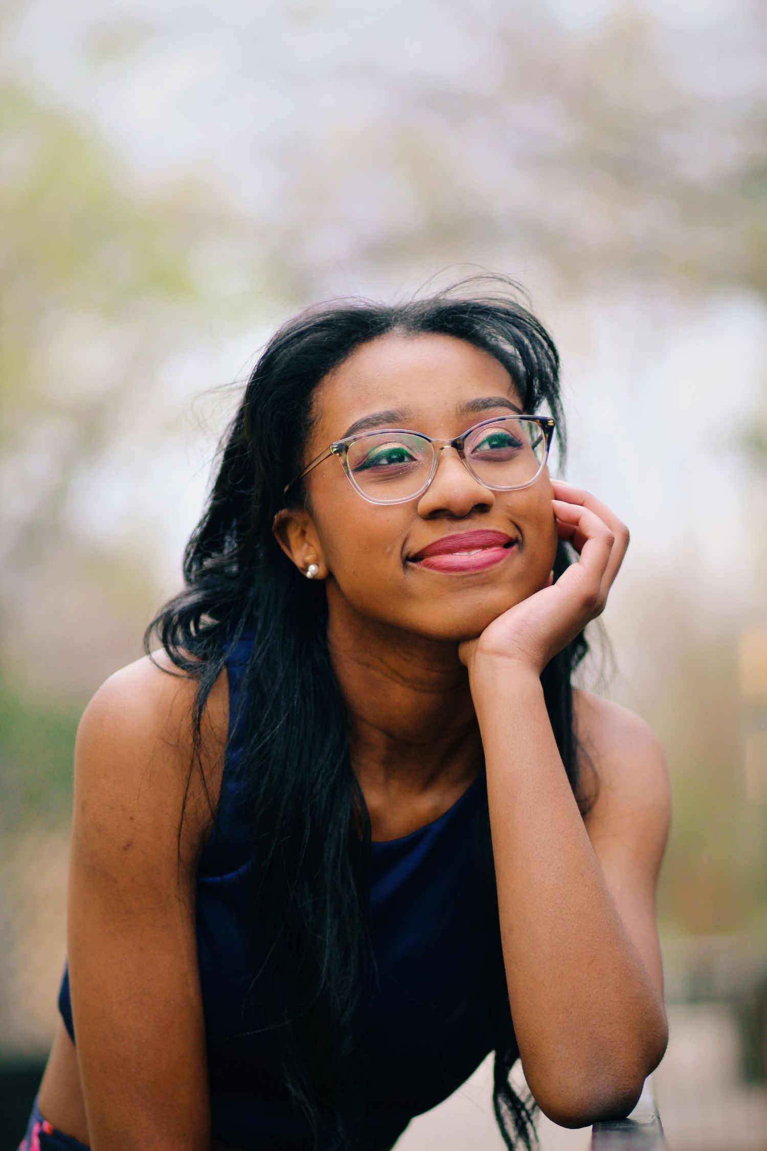 Outdoor portrait features glasses and genuine smile while resting head on hand.