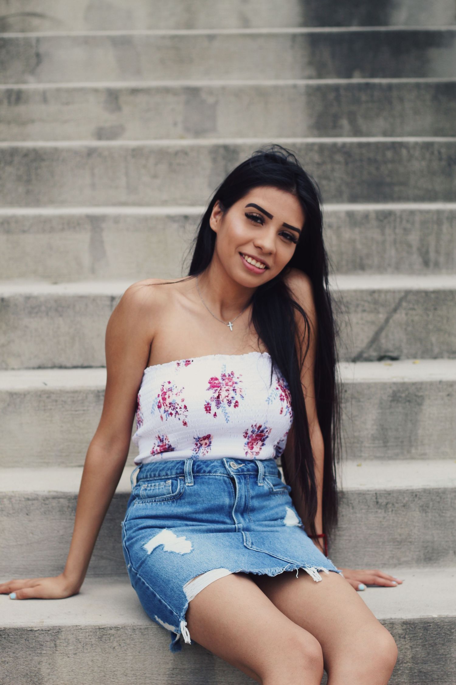 Summer portrait on concrete steps wearing floral top and denim skirt.