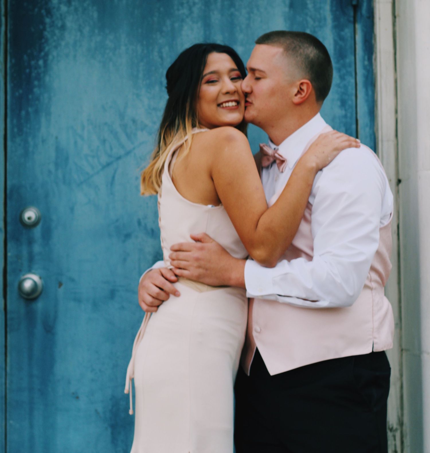 A couple embraces and smiles against a turquoise door background.