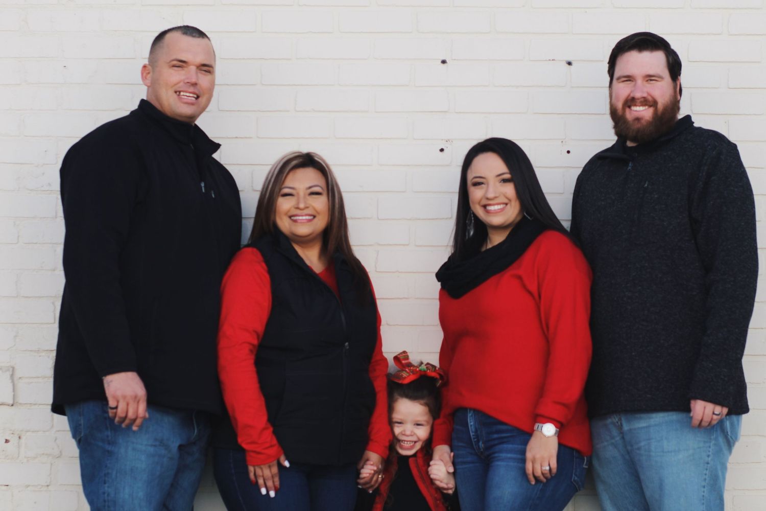 Family holiday portrait with four adults and child in red and black outfits against white wall.