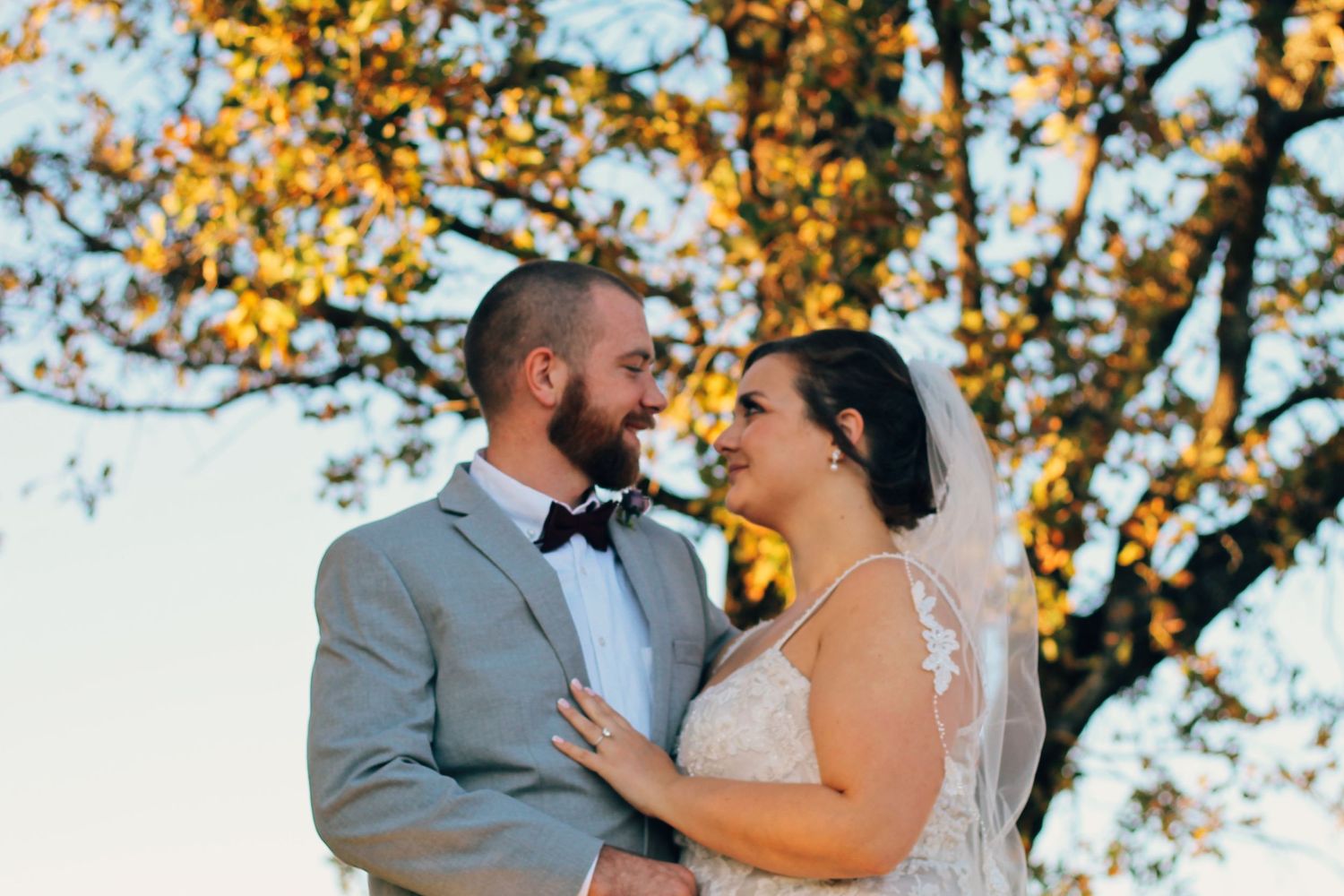 Bride and groom embrace during golden hour with autumn trees in background.