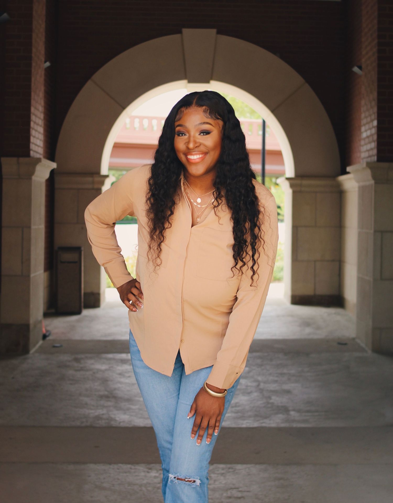 Portrait under an arched walkway wearing a beige blazer and ripped jeans.