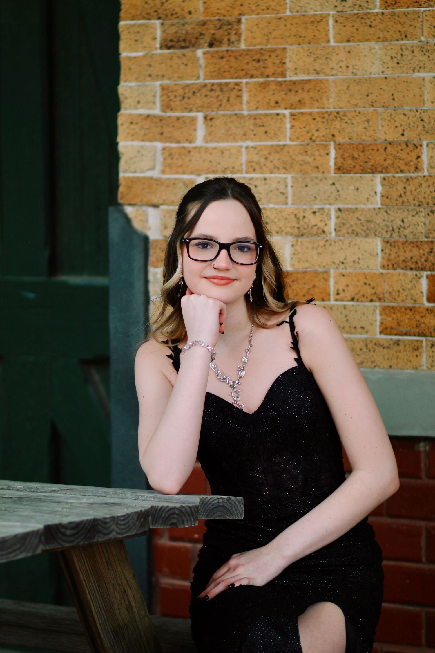 Elegant portrait in black dress and glasses against brick wall.