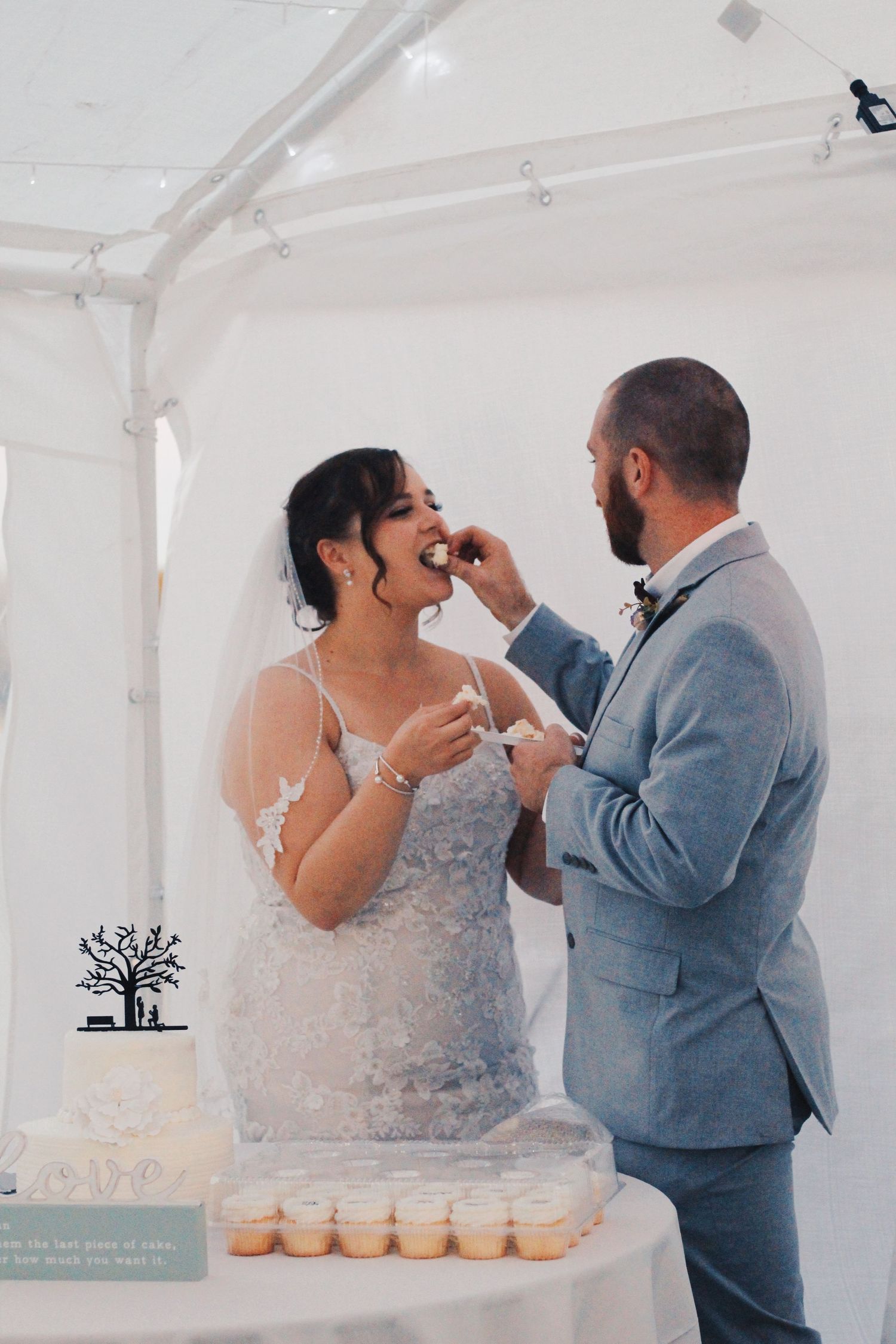Wedding couple sharing cake at their reception in a white tent.