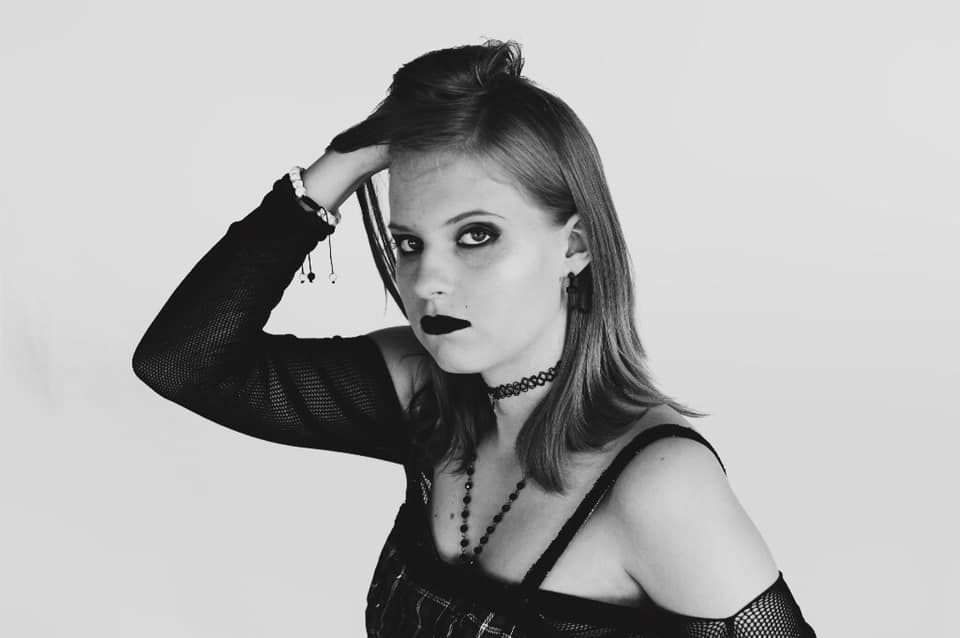 Black and white portrait of a gothic style model wearing dark lipstick and jewelry against light background.
