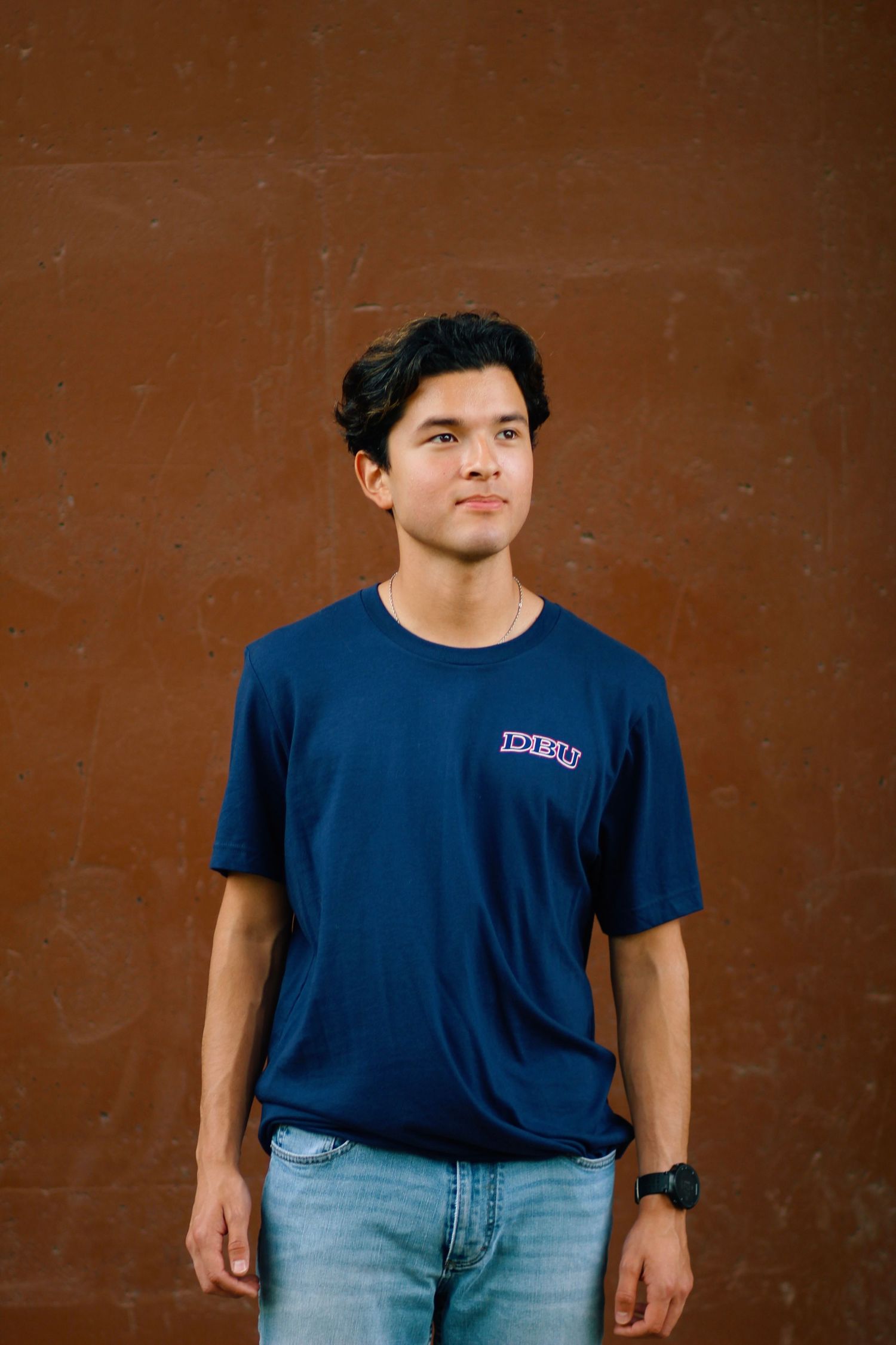 Casual portrait against brown wall wearing navy t-shirt and light denim jeans.