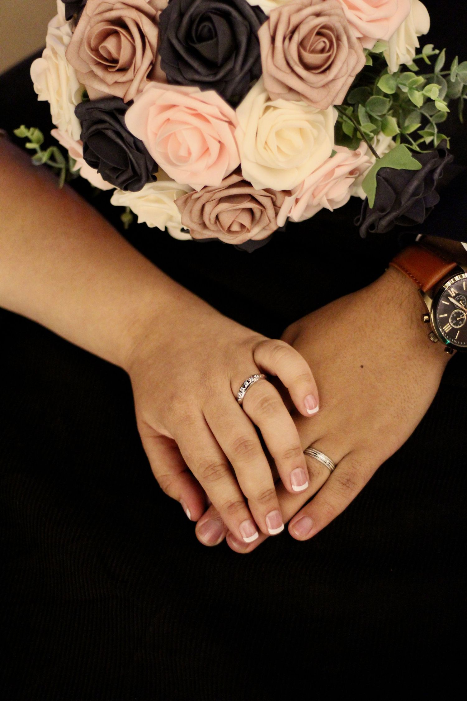 Close up of wedding rings with pink and dark roses bouquet in the background.