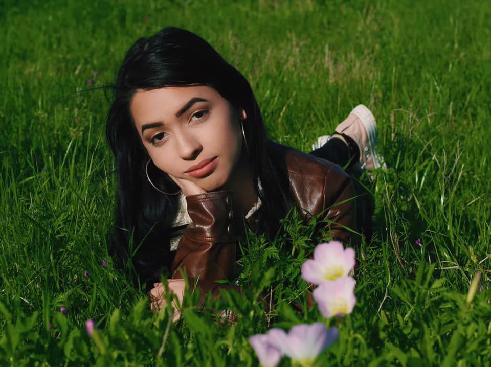 A person lying in green grass with pink flowers in a sunny outdoor setting.
