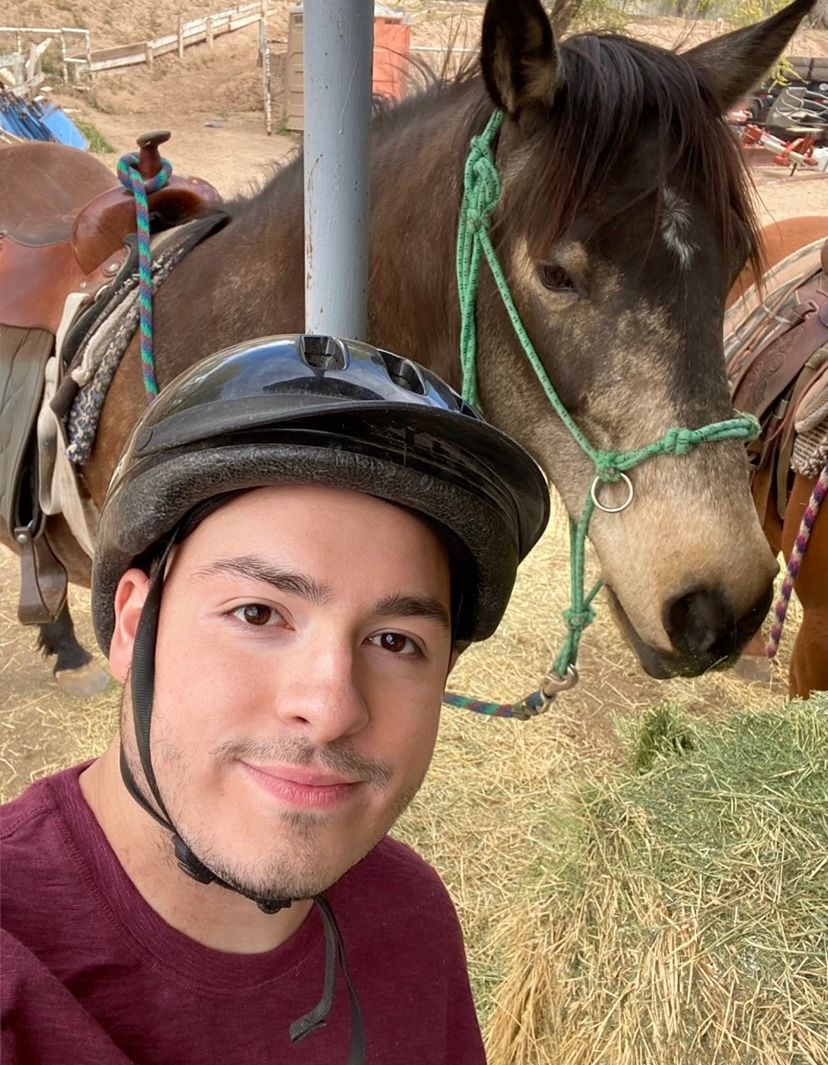 Horseback rider taking selfie with brown horse wearing green halter.