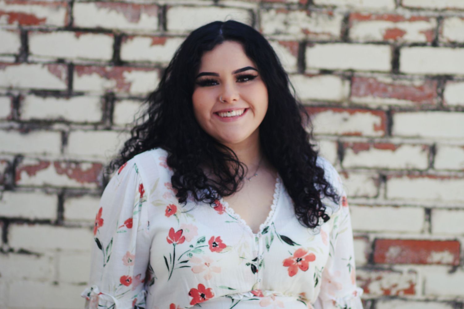 Portrait of person in floral print top against white brick wall.
