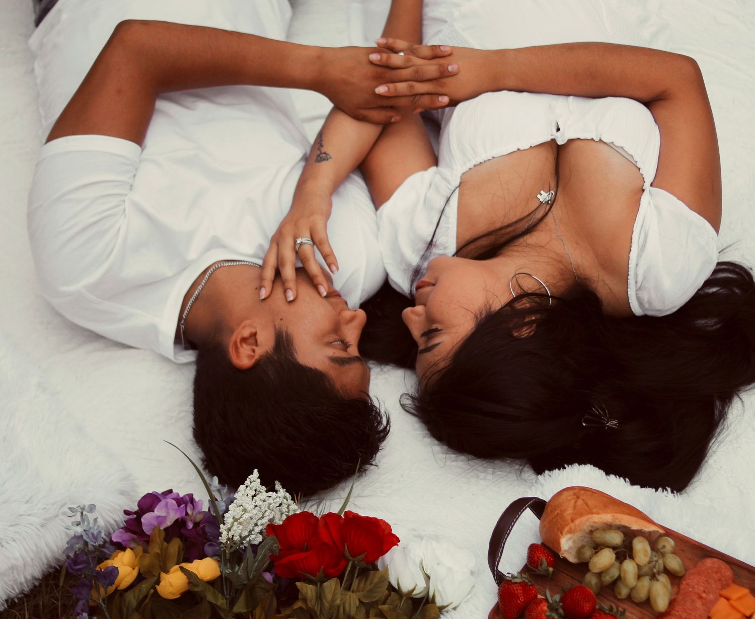 Artistic overhead shot of couple lying on white surface with flowers scattered nearby.