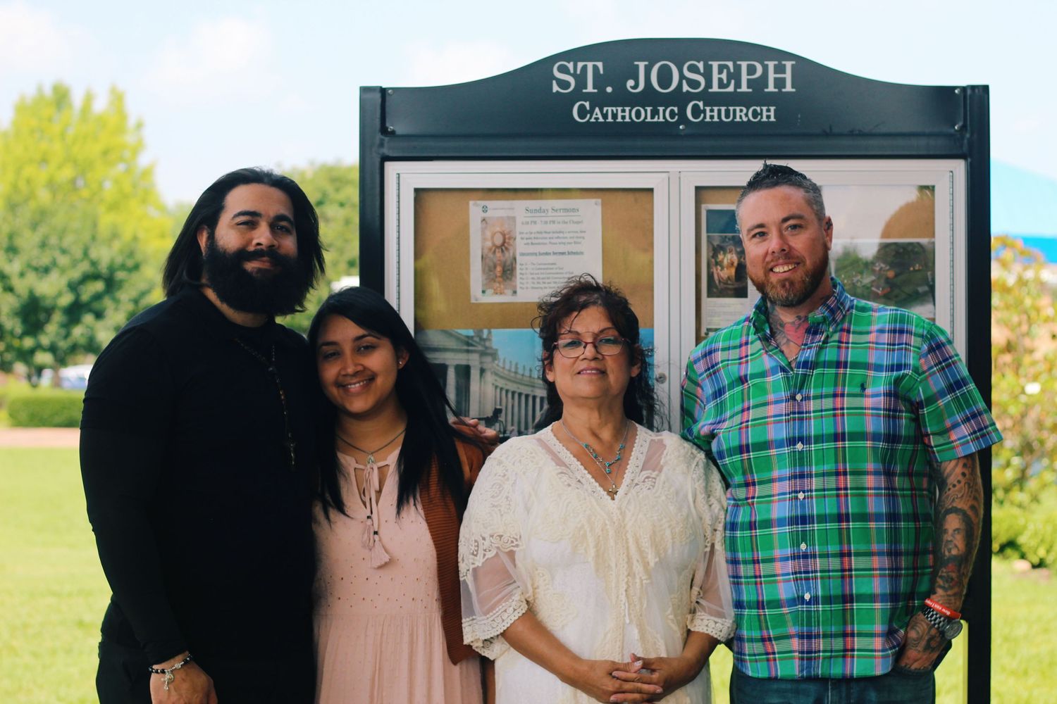 Group standing in front of St. Joseph Catholic Church sign on sunny day.