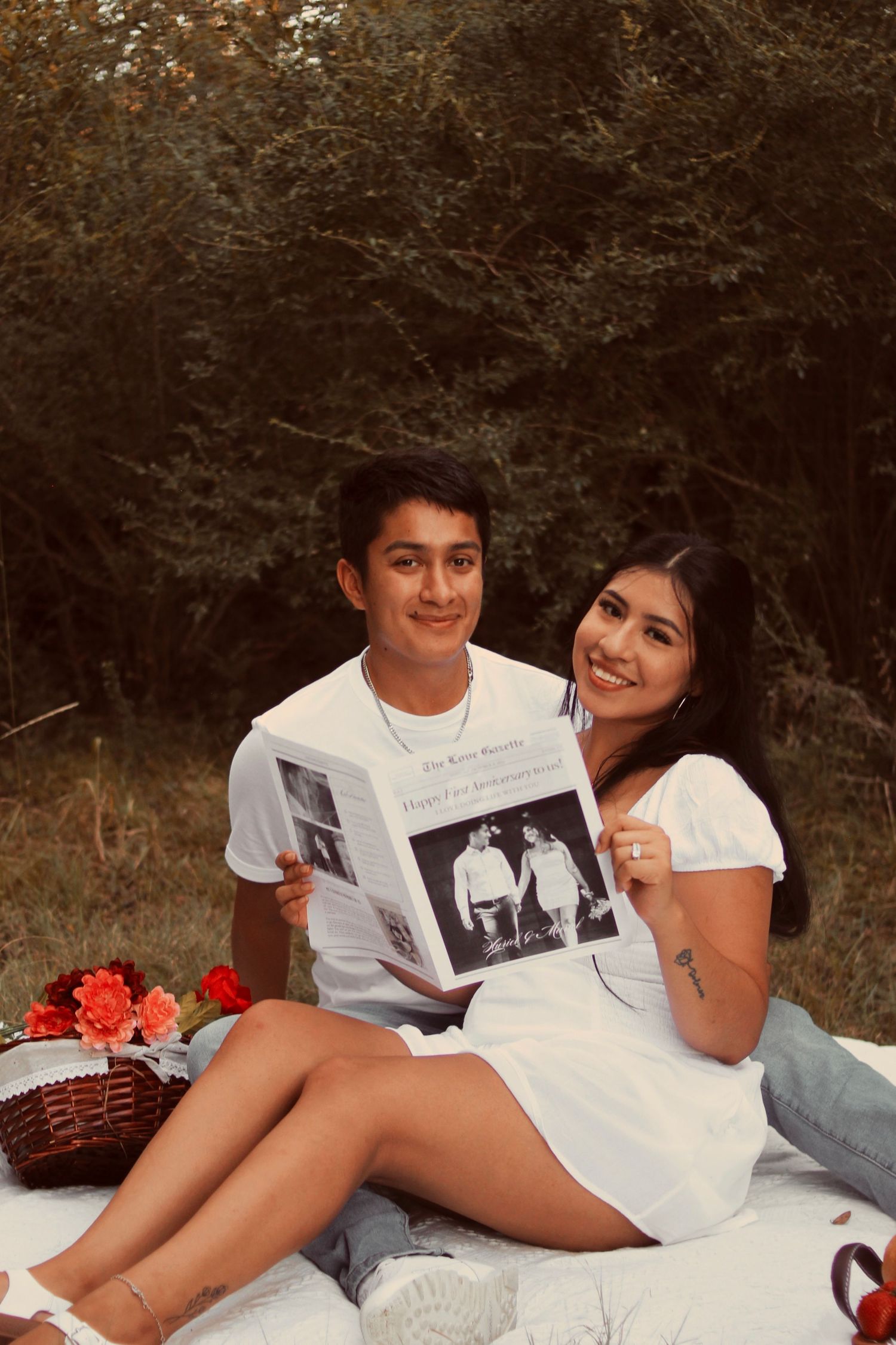 A couple enjoys a picnic on a blanket while looking at a photo album together outdoors.