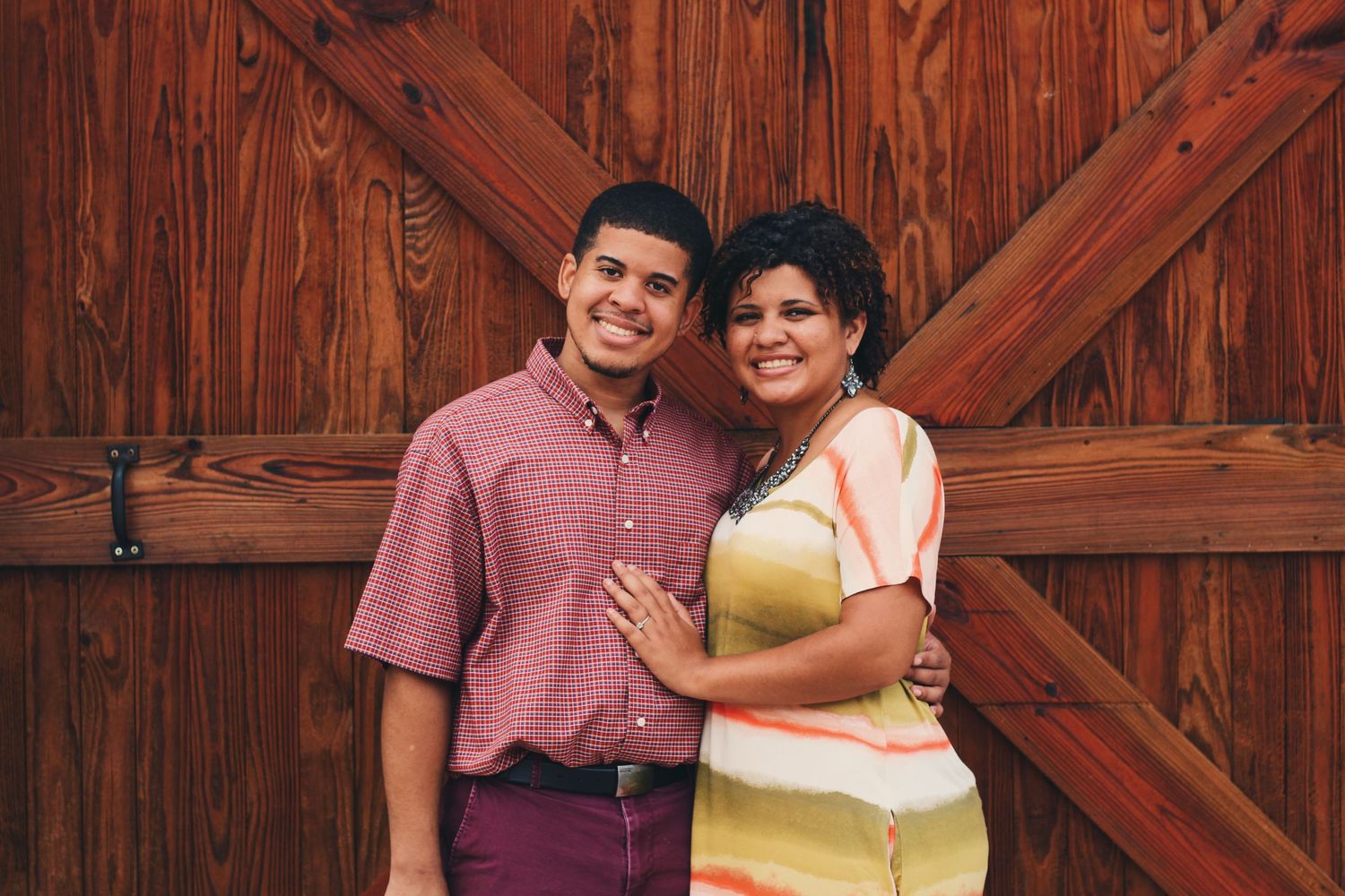 A happy couple embraces while standing in front of a wooden barn door.