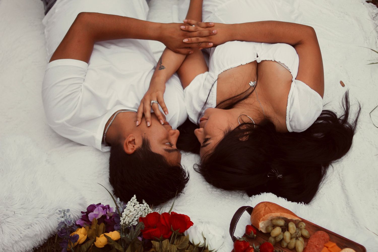 Artistic overhead shot of two people lying on white bedding with flowers.