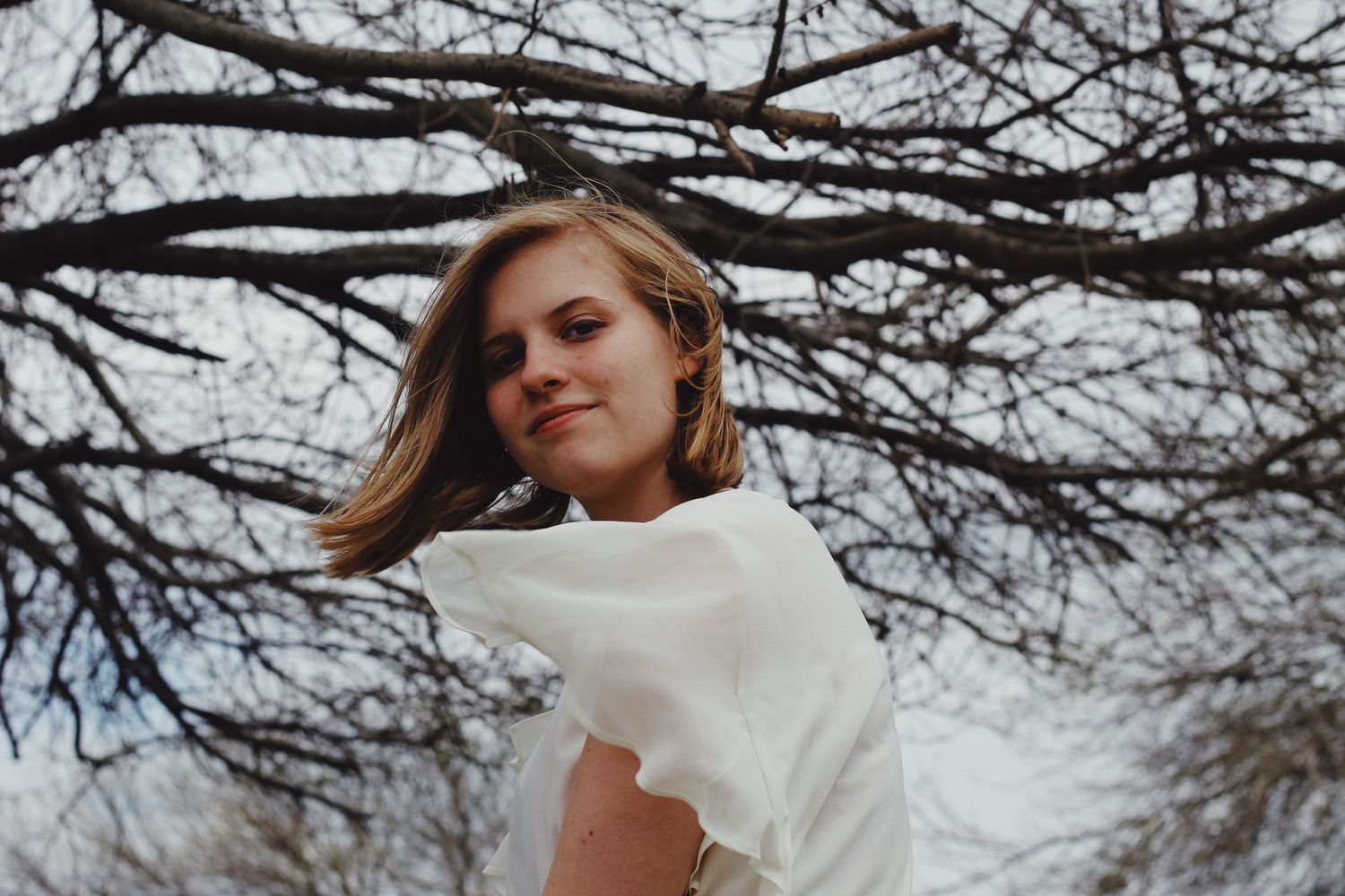 Person in white top turns head against winter tree branches background.