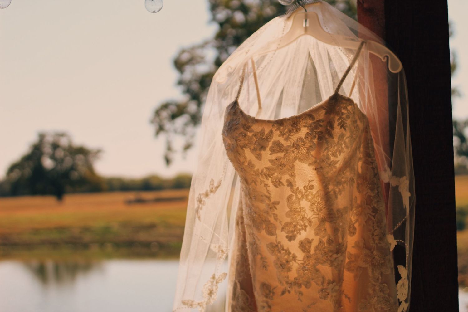 Vintage-style gold and beige wedding dress hanging against a sunset lake backdrop.