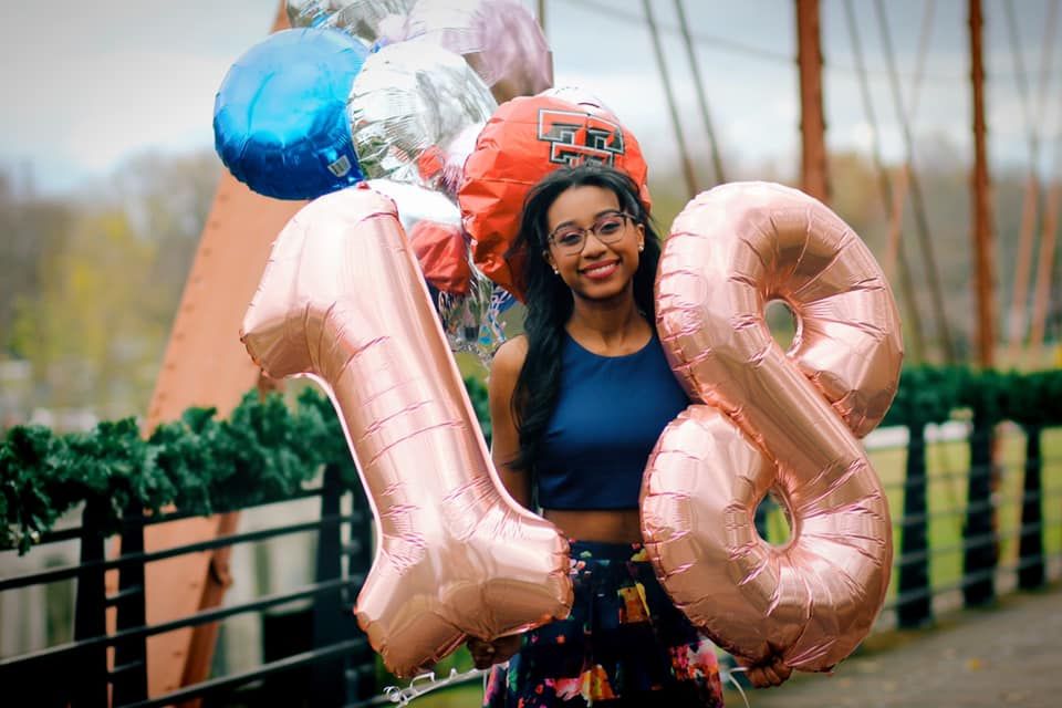 Person holding large rose gold number balloons celebrating milestone birthday outdoors.