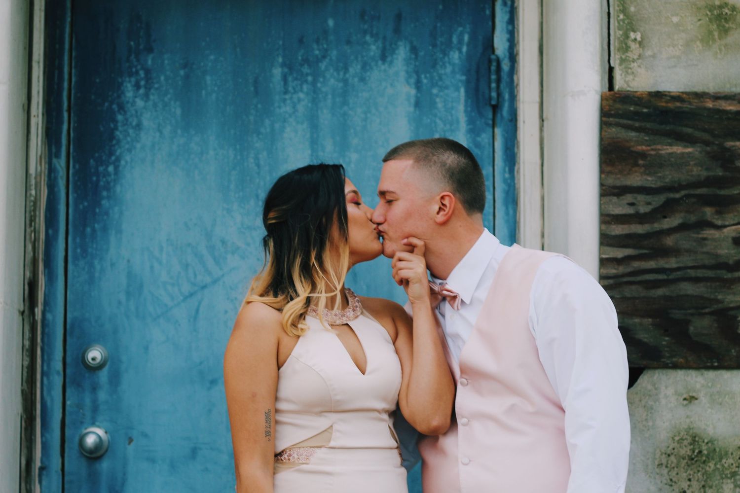A couple shares an intimate moment in front of a bright blue door.