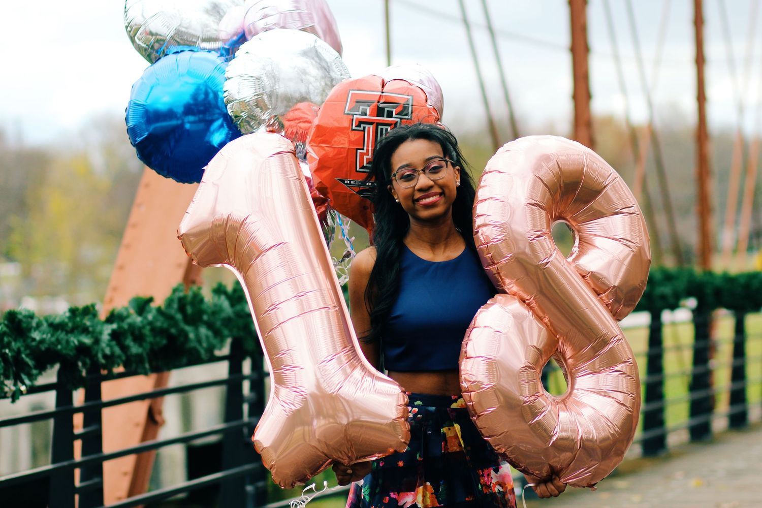 A celebratory photo with someone holding large metallic number balloons on a bridge.