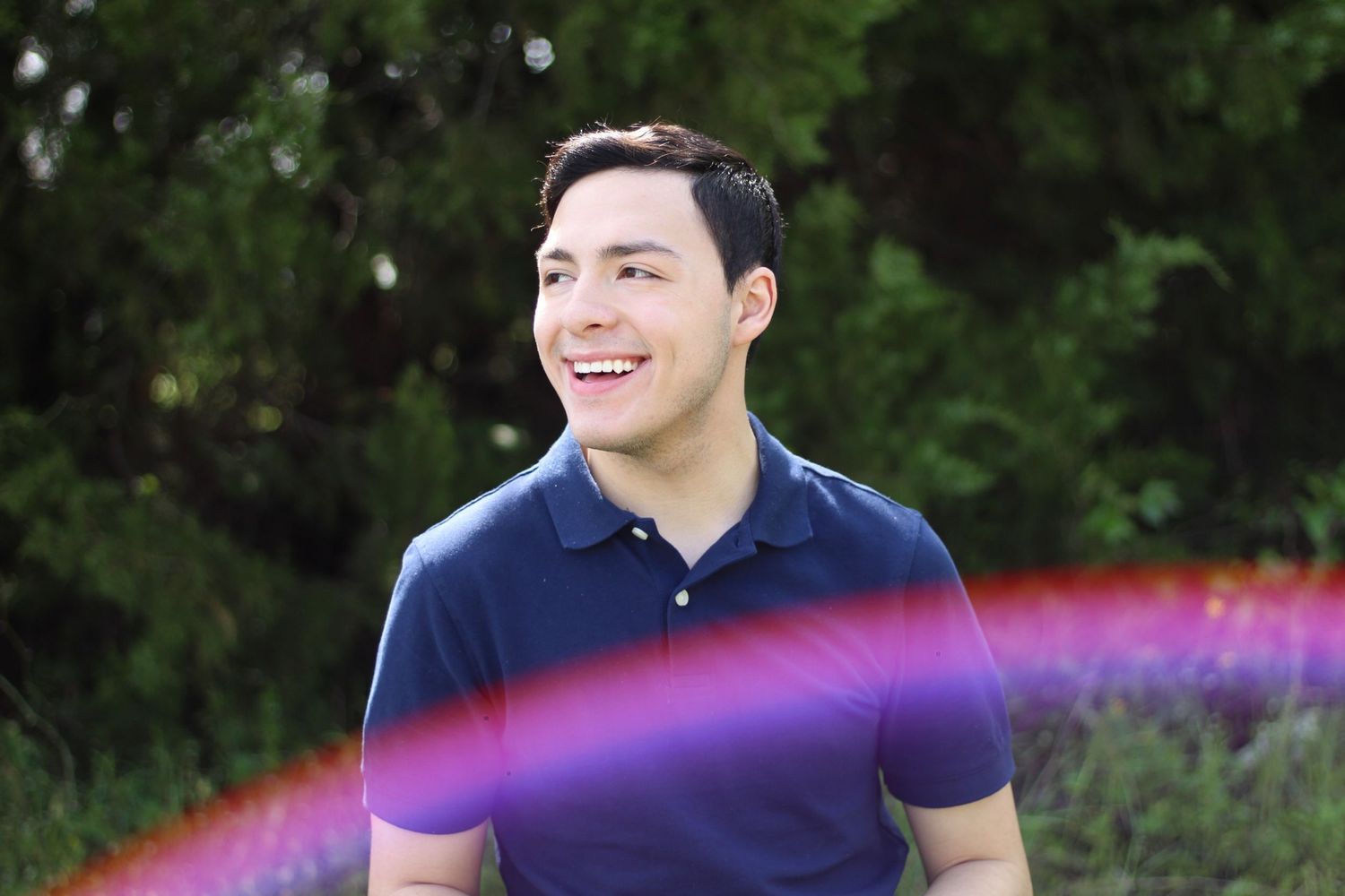 Person in navy polo shirt with colorful rainbow light effect outdoors.