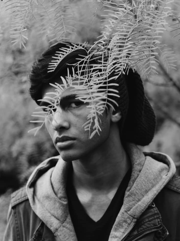 Moody black and white portrait with delicate fern fronds casting shadows on the subject.