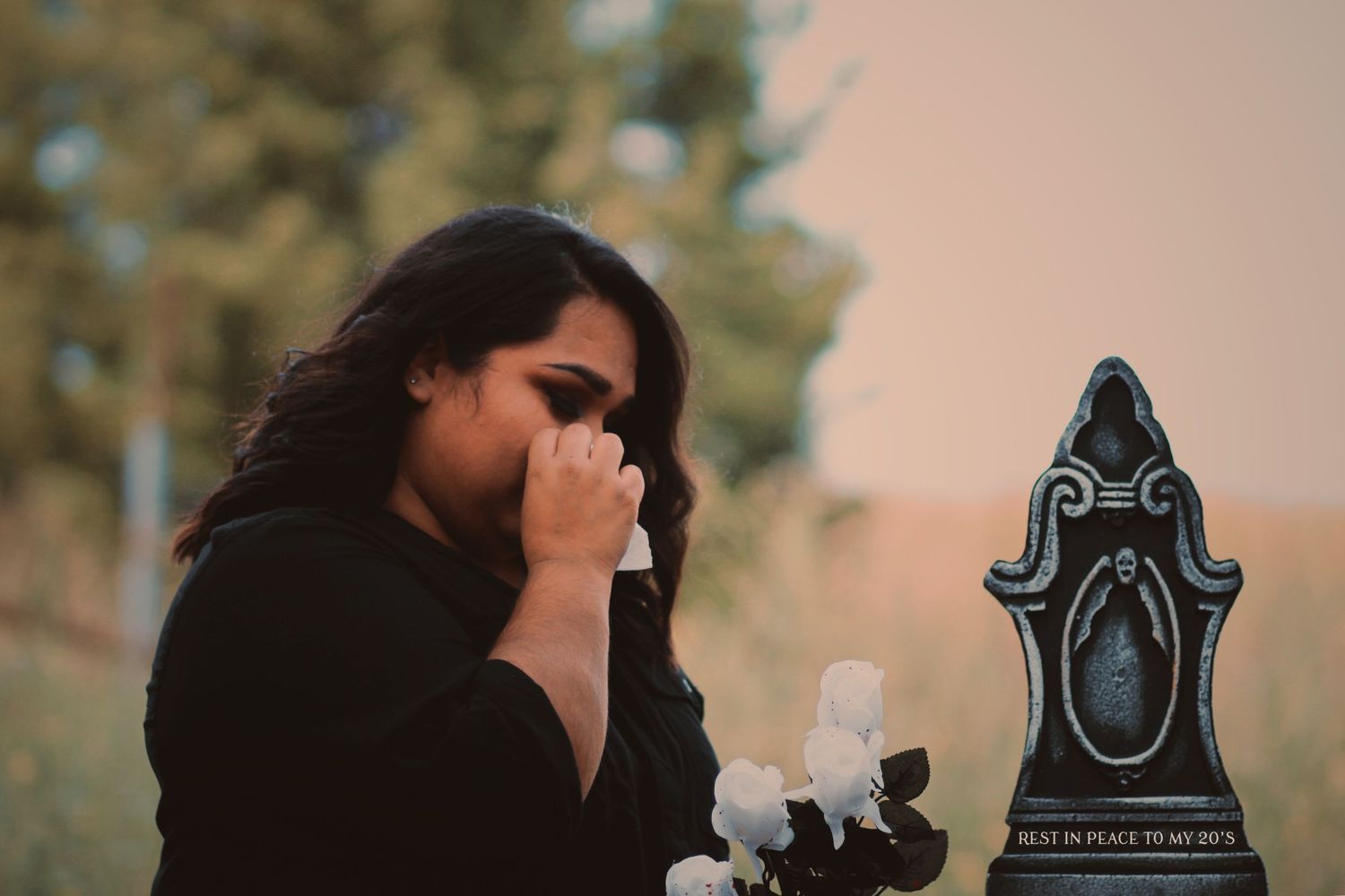 A person in black performs a witchy photoshoot with candles and a decorative gravestone.