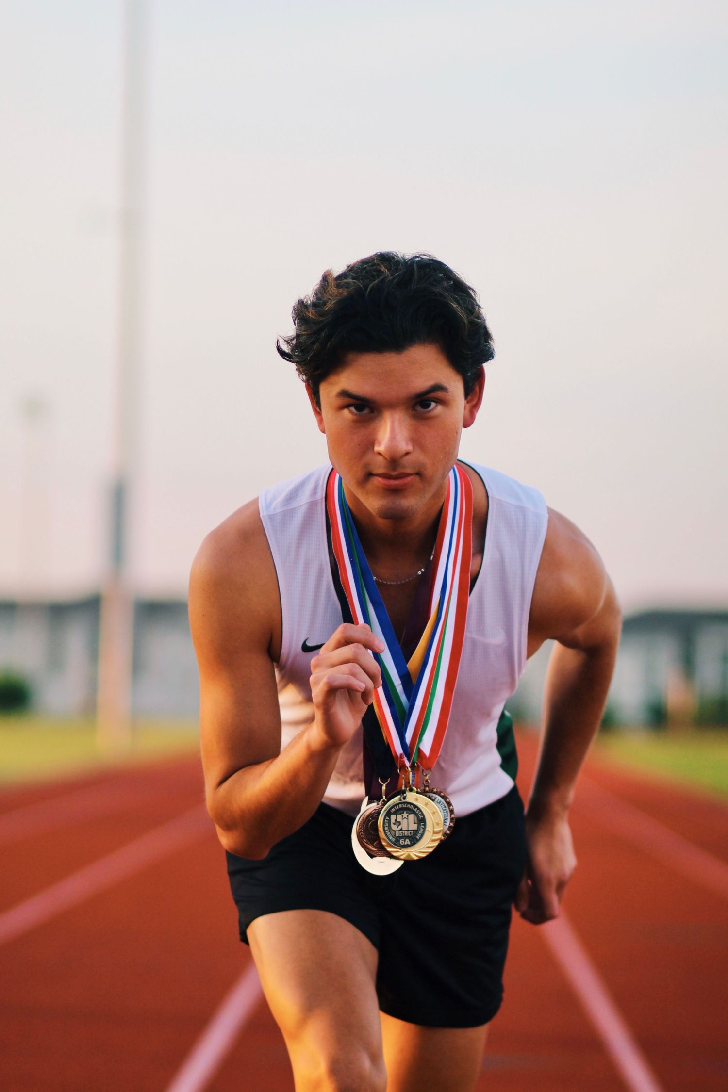 Athlete on running track wearing medals and athletic gear.