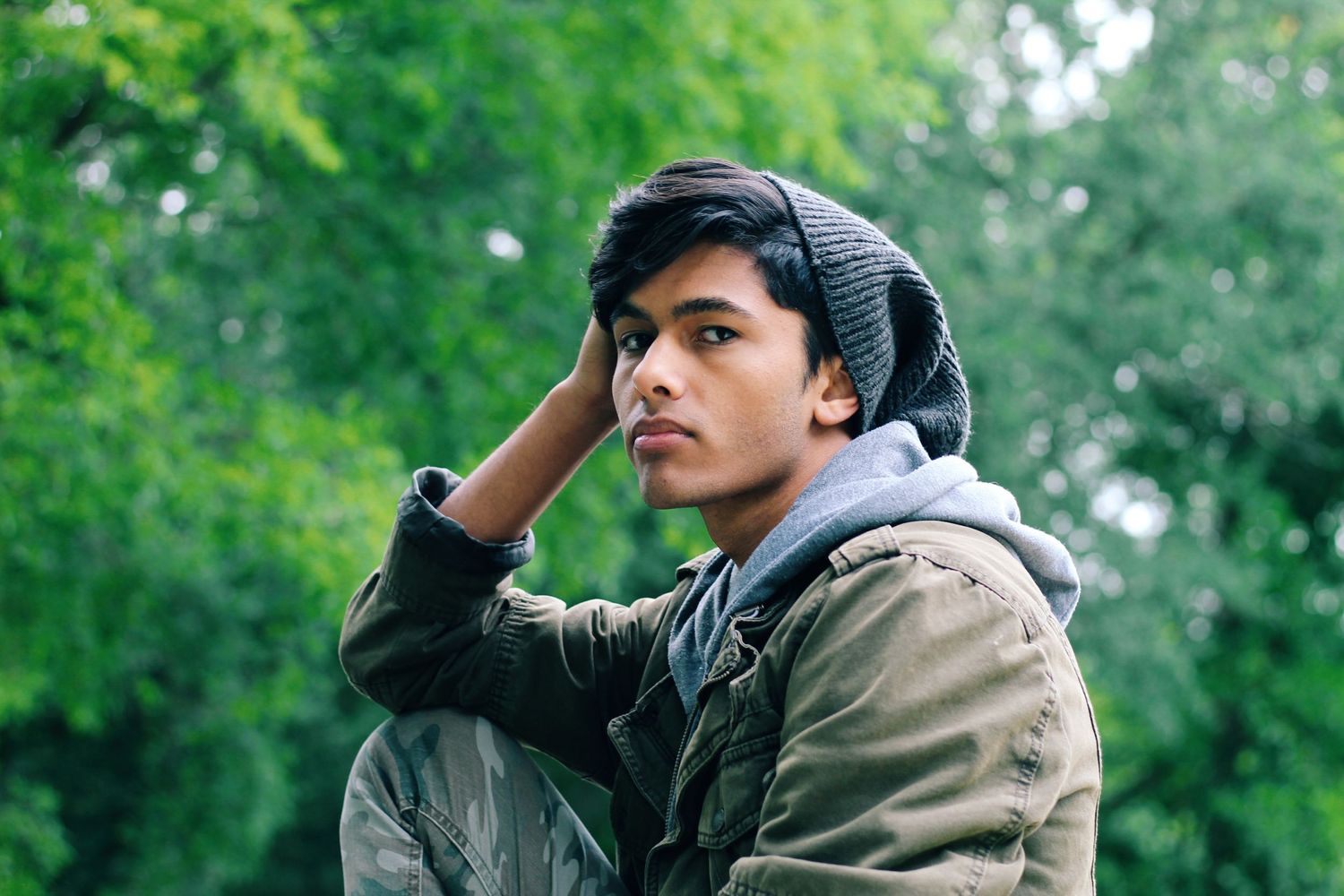 Outdoor portrait wearing beanie and jacket against green foliage.