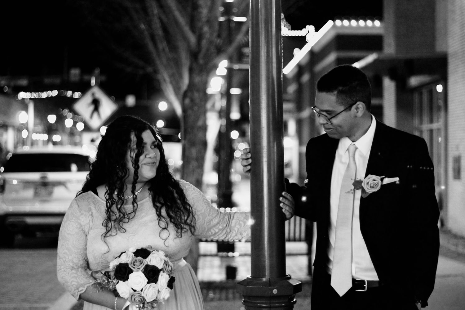Couple sharing a candid moment on a city street at night with bouquet.