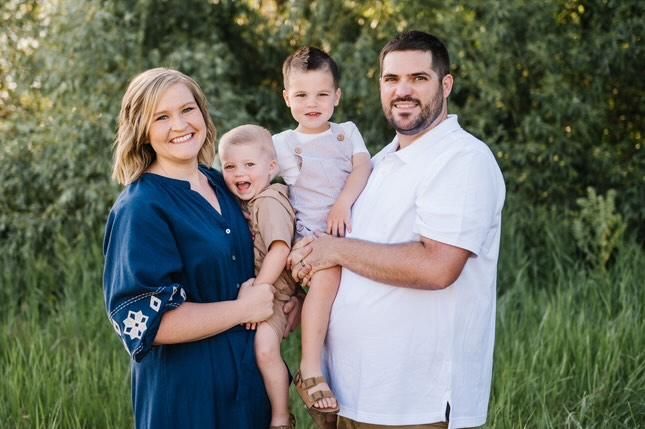 A family stands together outdoors in navy and white clothing against a natural green background in summer.