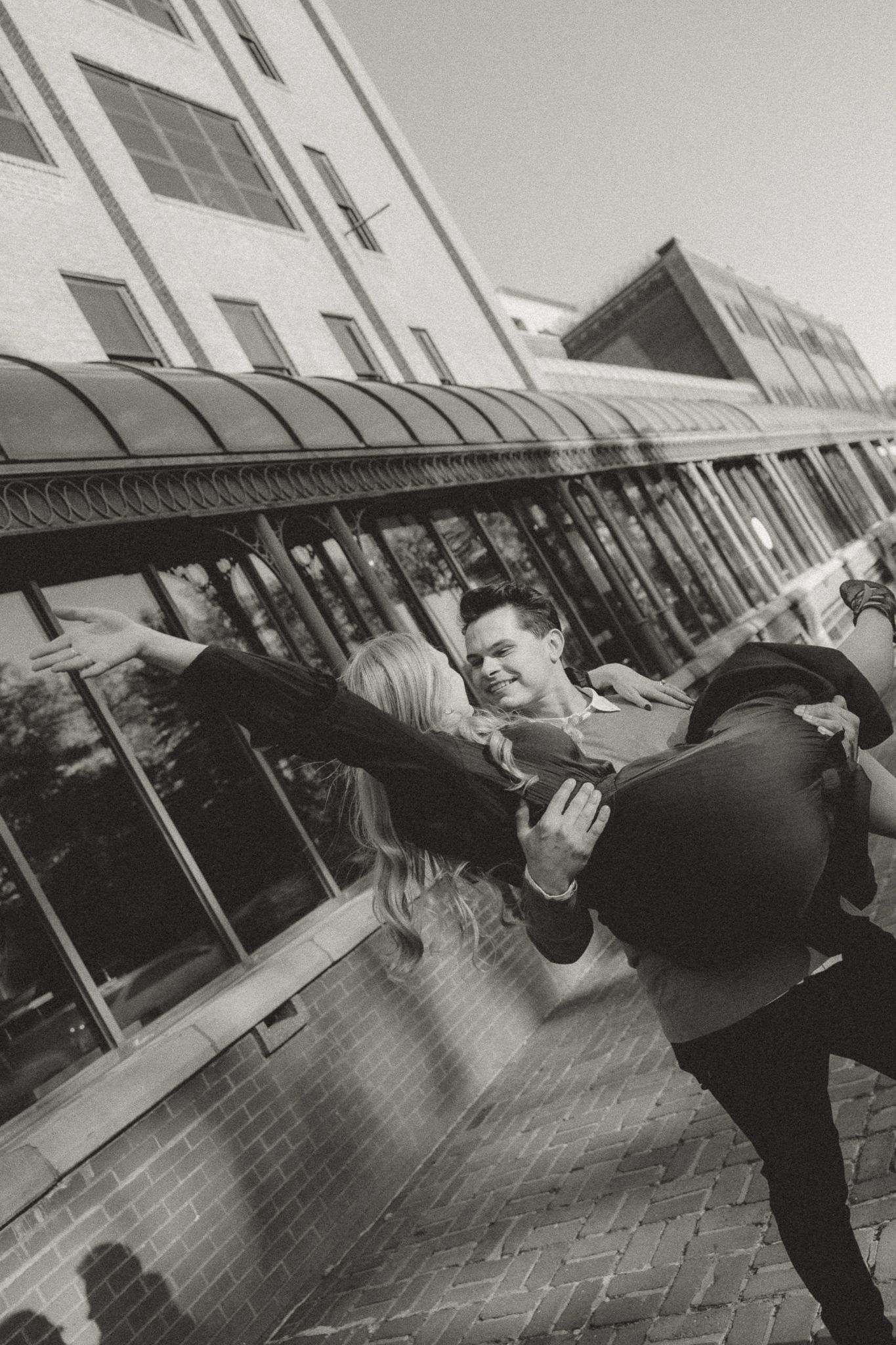 Artistic black and white sequence of couple posing playfully against modern architecture.