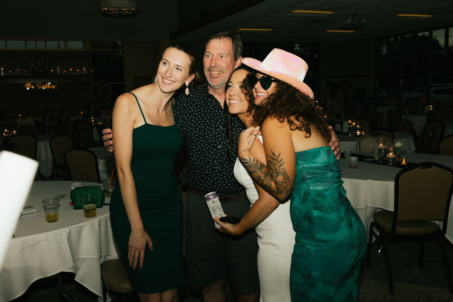 Party guests pose together at an event while holding drinks and wearing formal attire.