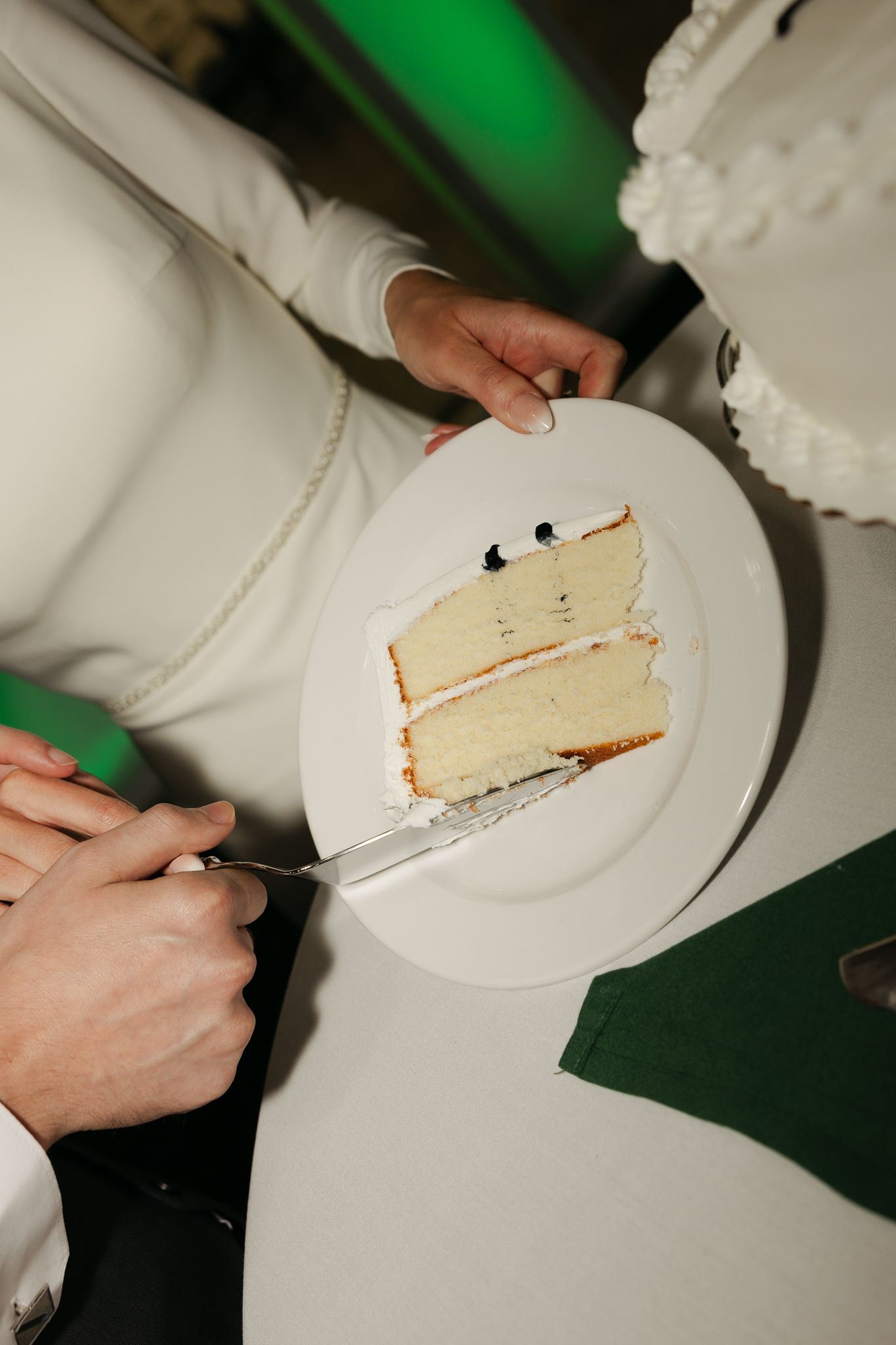 Close-up of hands cutting and serving slices of white wedding cake.