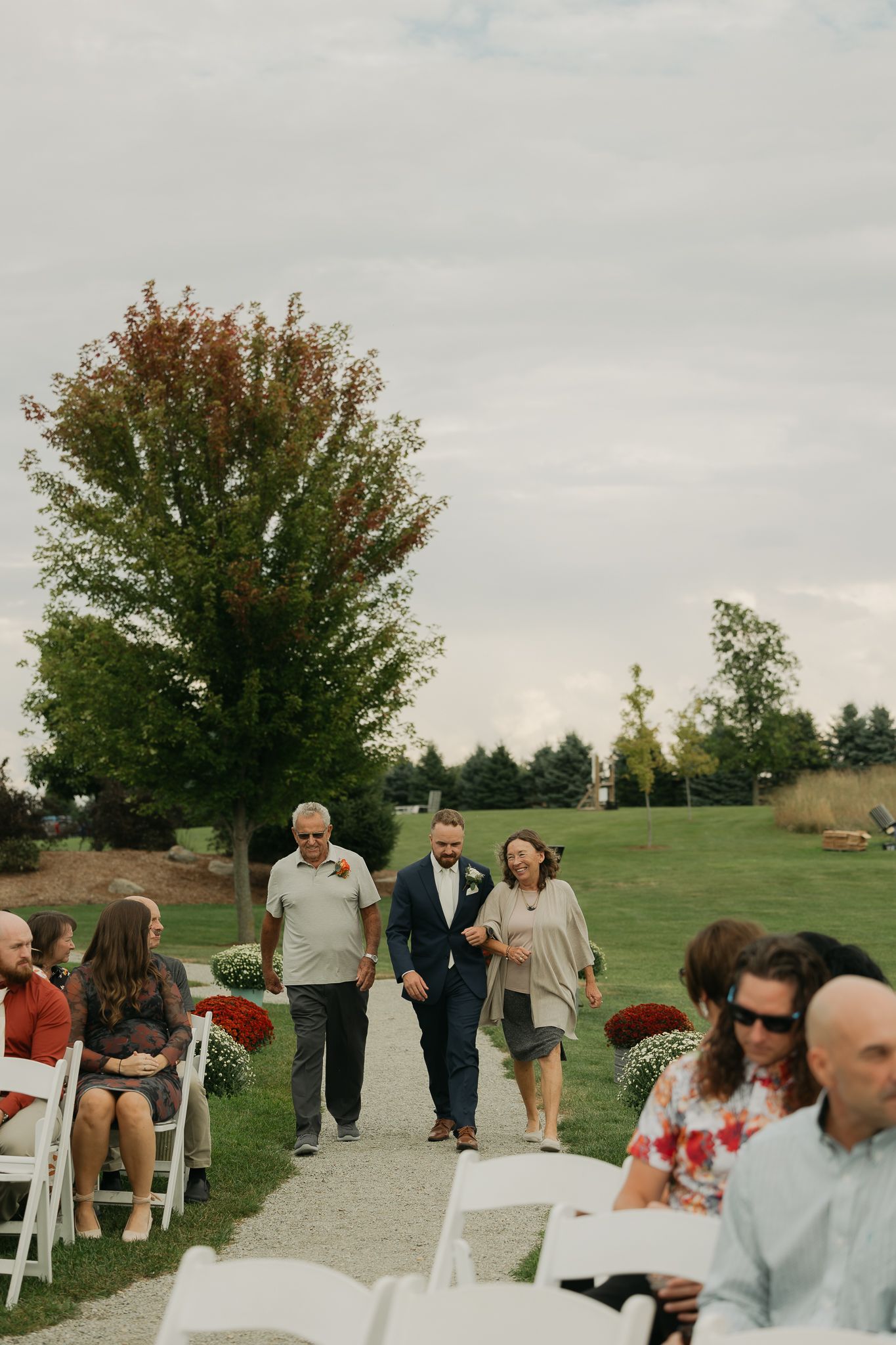 Guests seated in white chairs for an outdoor wedding ceremony on a grassy hillside.
