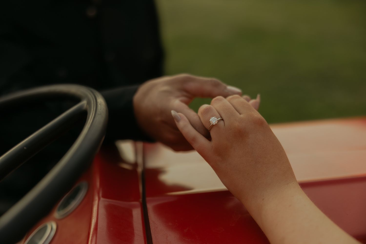 Close-up shot of hands resting on a red surface with a wedding ring visible.