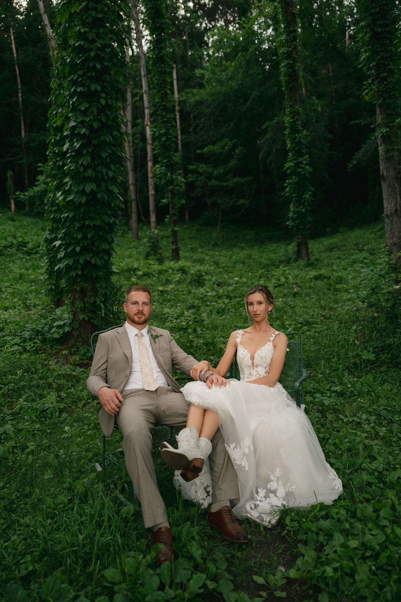 Couple in wedding attire sitting together in a peaceful forest setting.