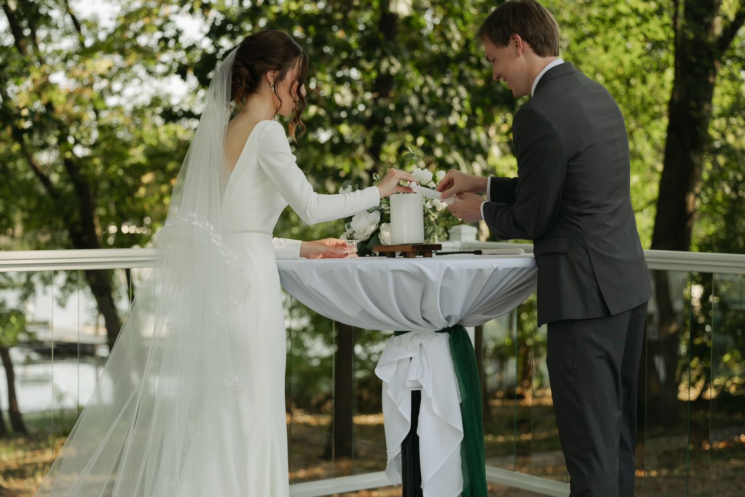 Wedding ceremony participants gather under an outdoor pergola surrounded by trees.