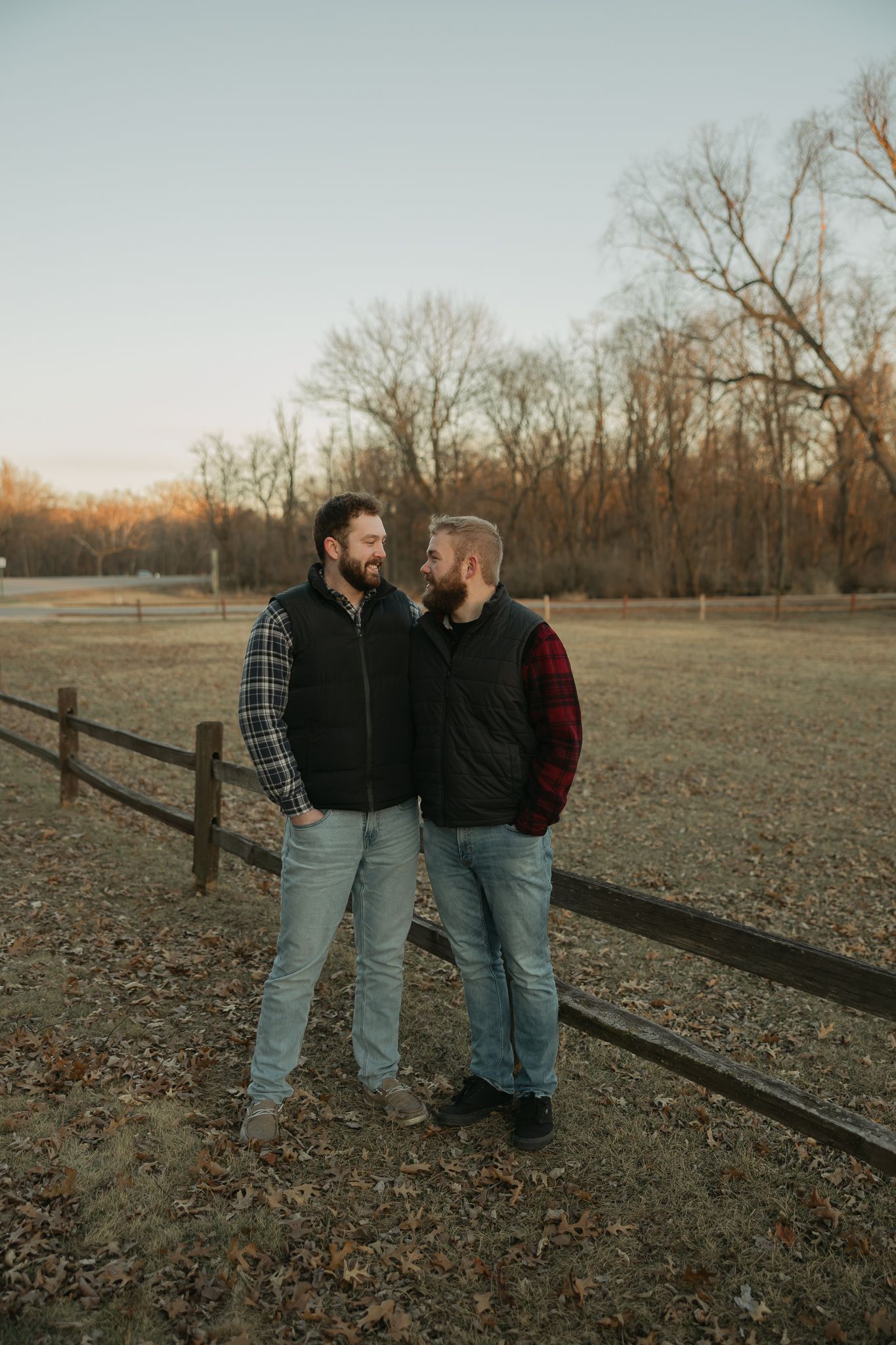 Couple sharing intimate moments together by a rustic wooden fence at sunset in an autumn field.