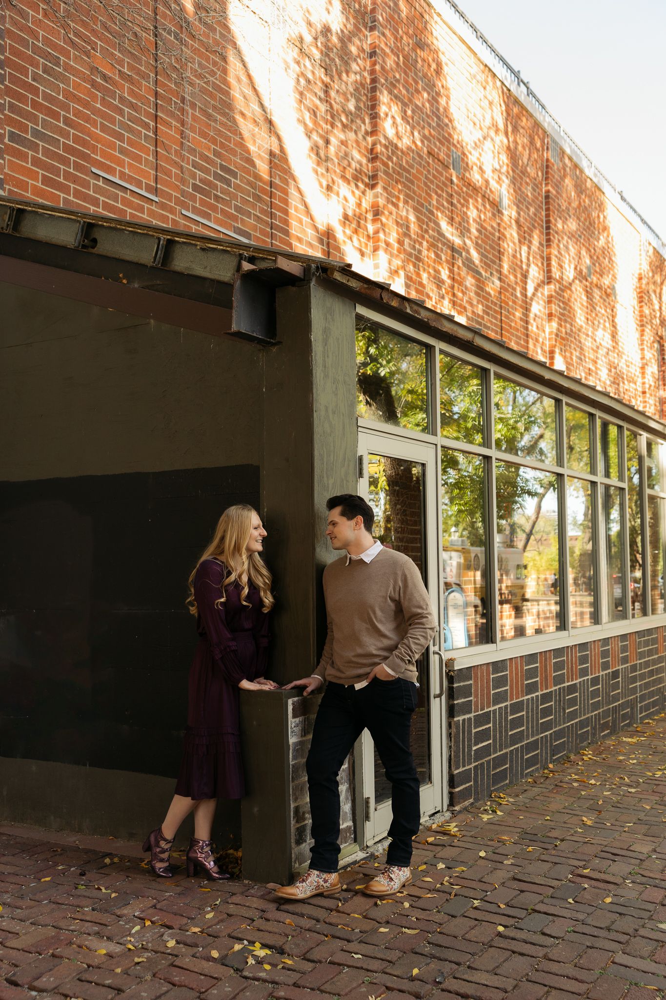 A couple having a tender moment against a brick wall exterior with windows.