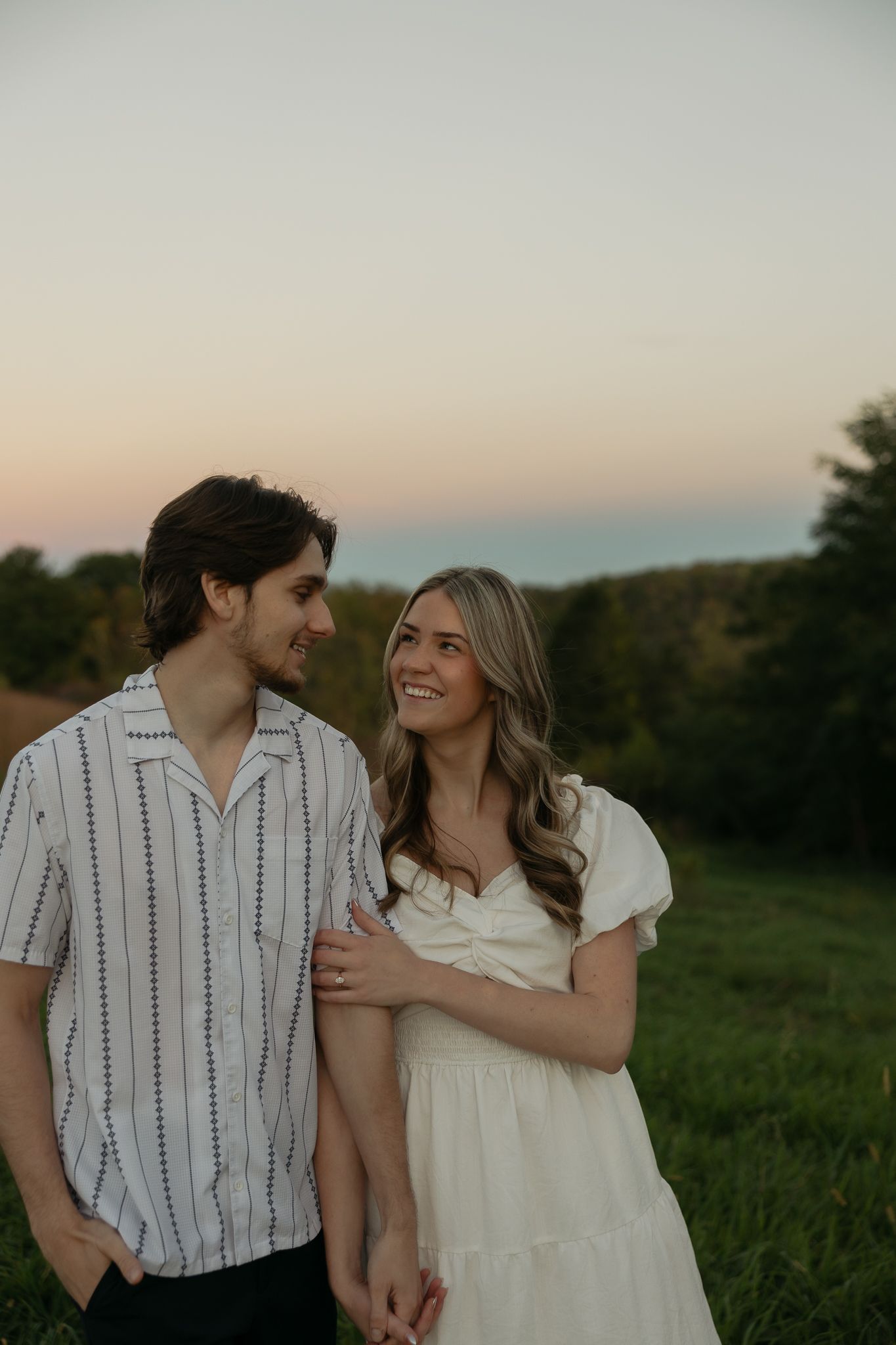 A couple shares a joyful moment together at sunset in a grassy field.