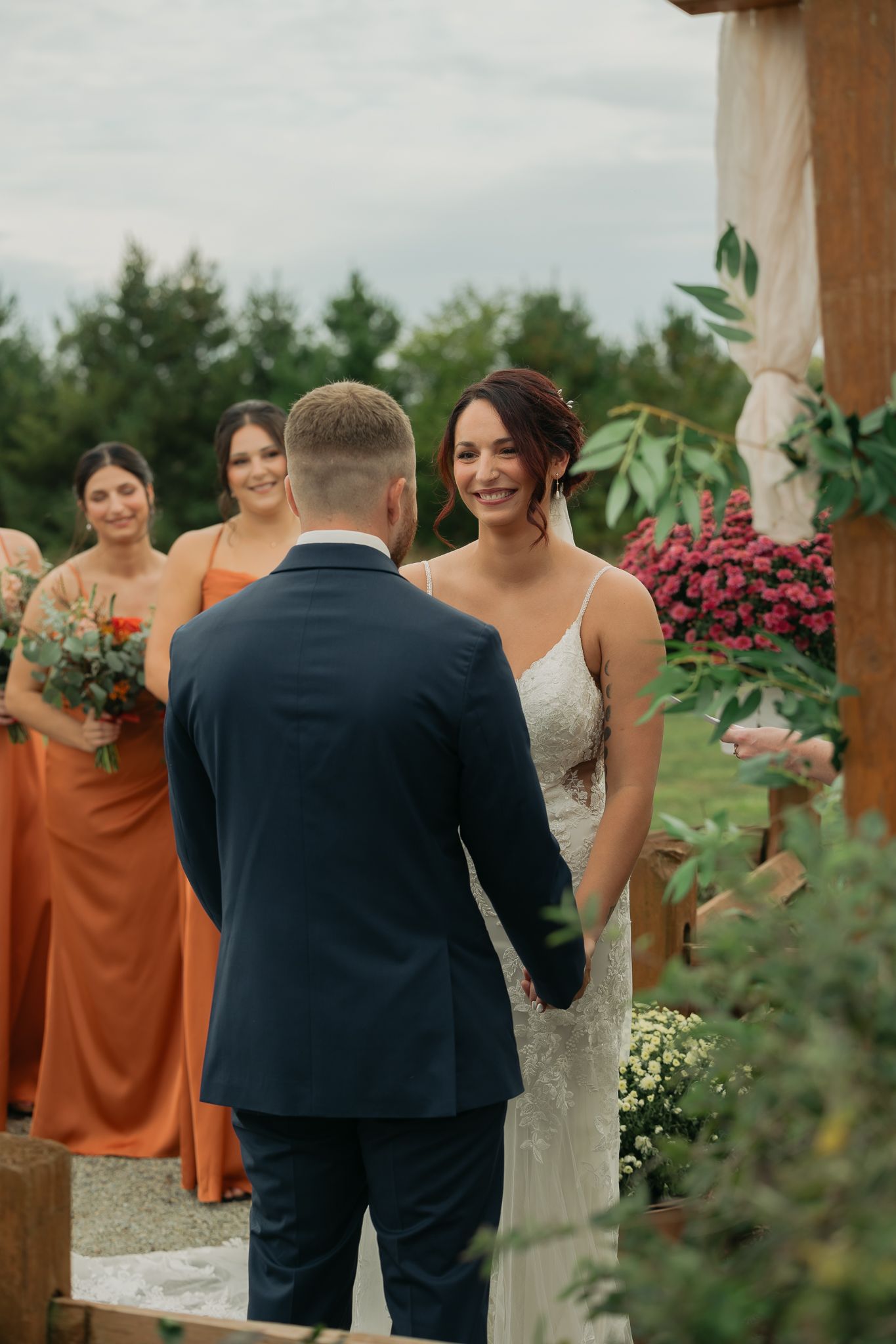 Wedding ceremony under wooden pergola decorated with greenery and white fabric.