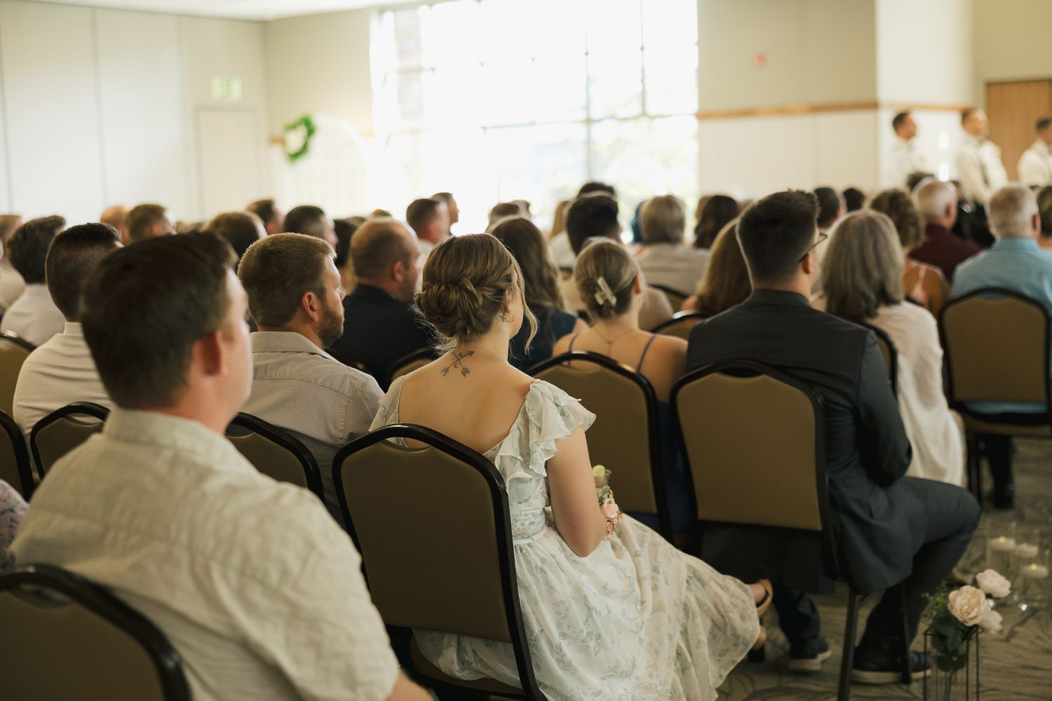 Wedding guests seated in rows at an indoor reception venue.