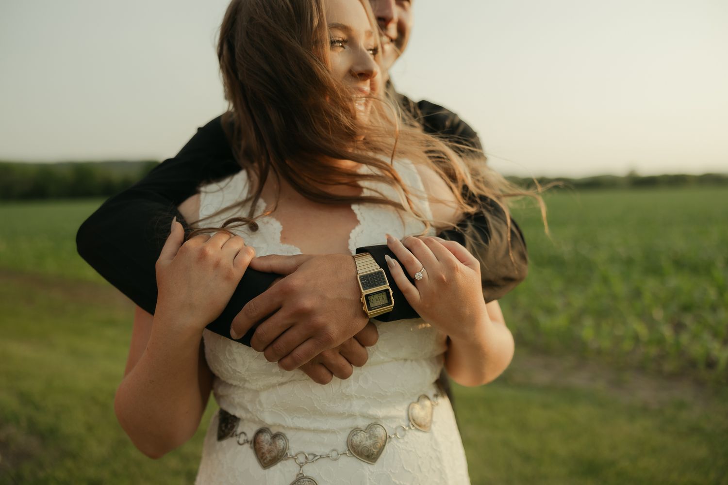 A tender embrace captured in a sunlit field with rolling farmland in the background.