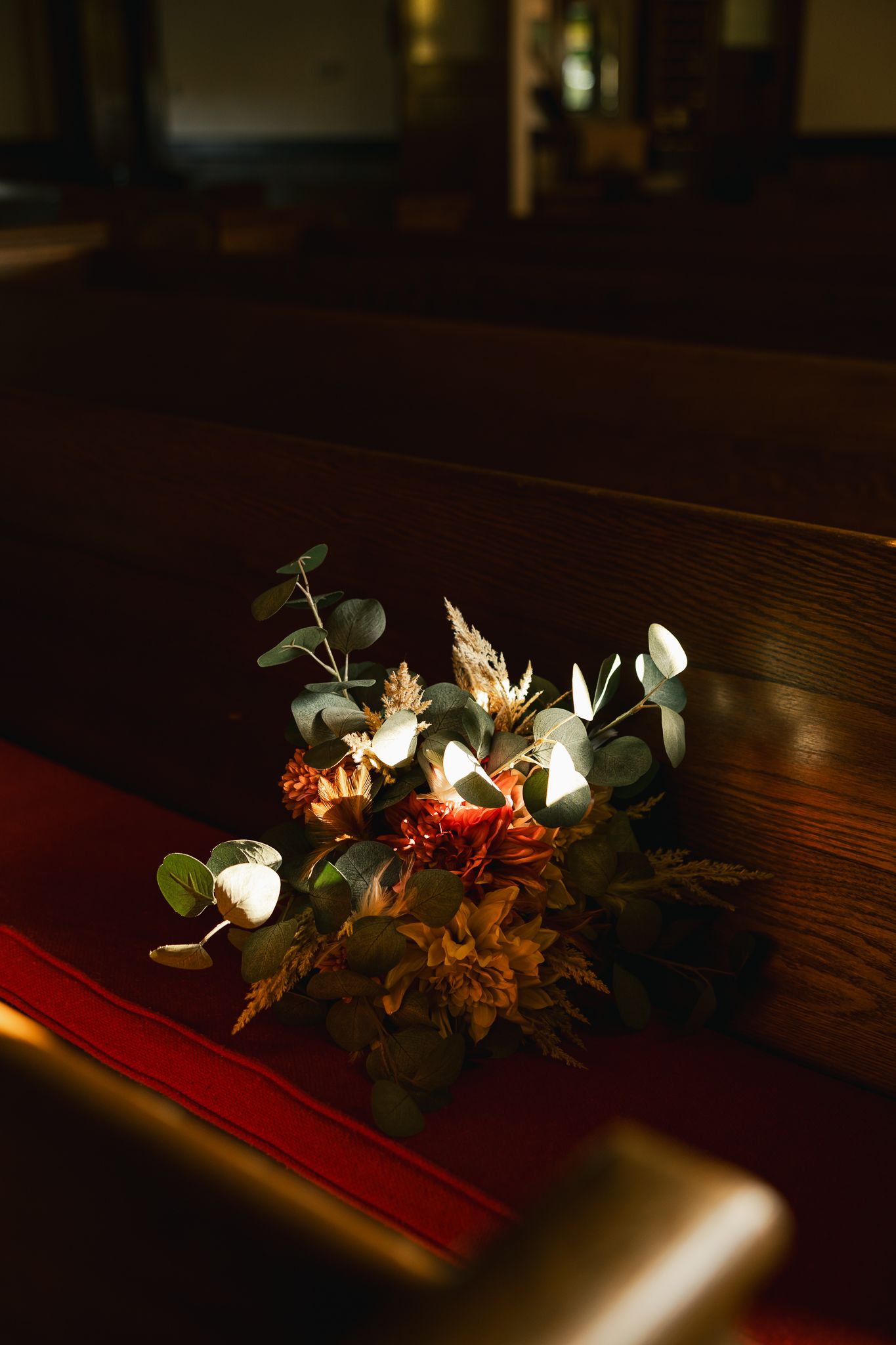 Elegant floral arrangement with white flowers and greenery on dark wooden surface in low light.