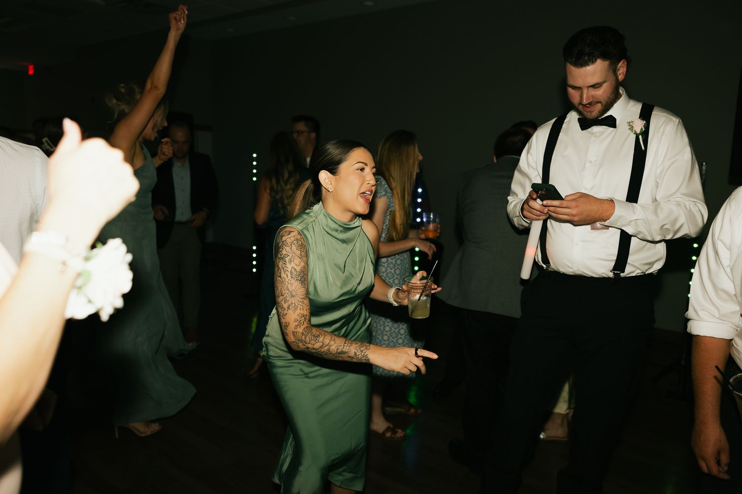 Wedding party guests dance and celebrate on a dark dance floor.